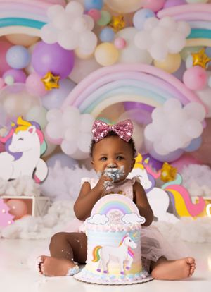 Magical unicorn cake smash setup with pastel balloon clouds and rainbow decorations.