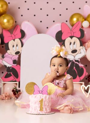 Pink Minnie Mouse themed cake smash photo session with gold balloons and polka dot backdrop.