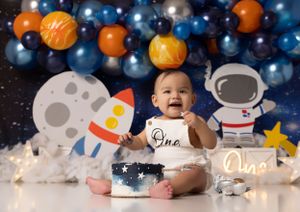 Space themed cake smash photography setup with blue and orange balloons against dark backdrop.