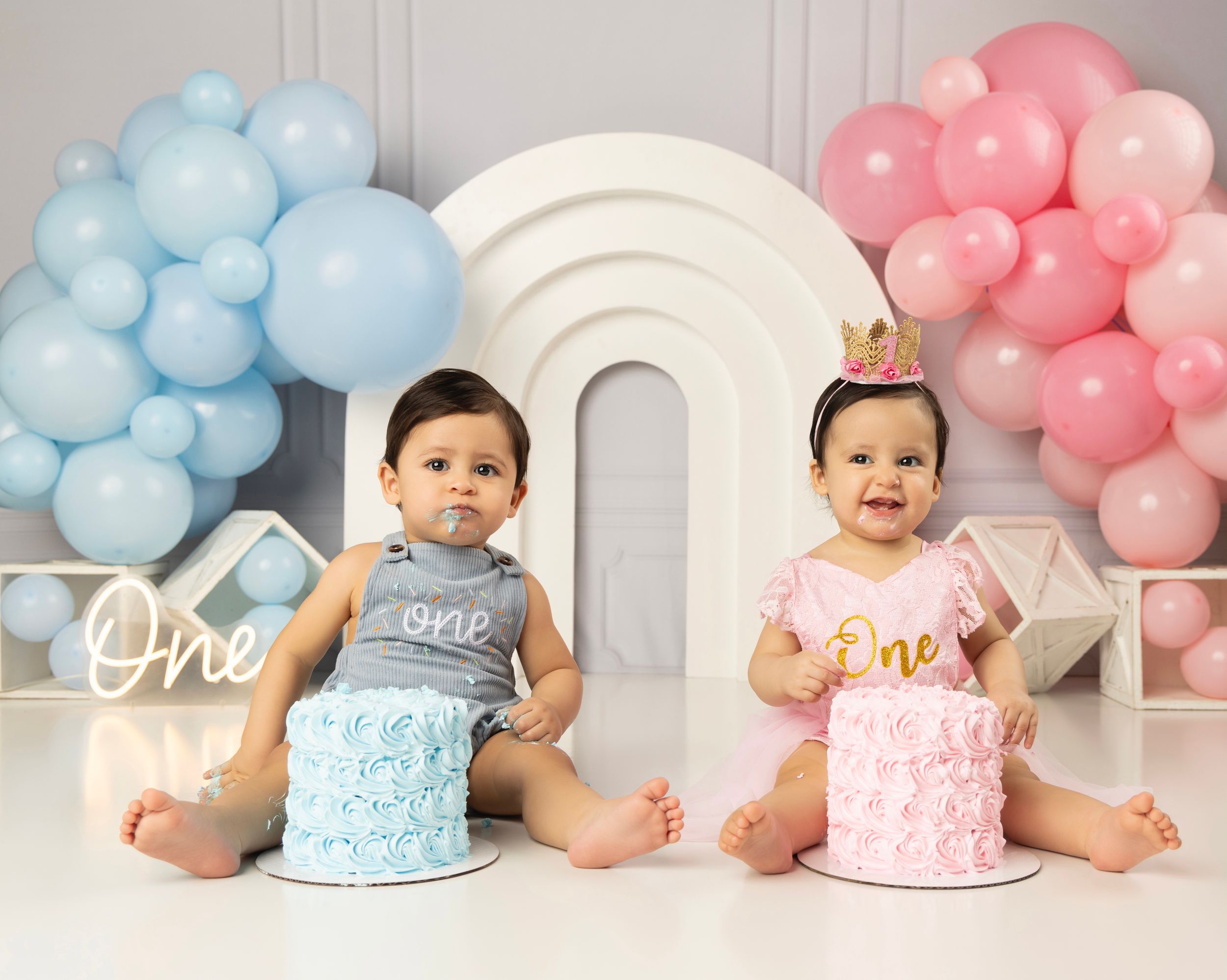 Baby cake smash photo series with pink and blue balloons and matching cakes.