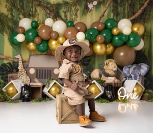Safari-themed first birthday setup with green and gold balloon arch and decorative props.