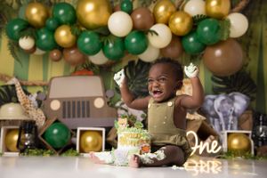 Joyful baby celebrating first birthday with green and gold balloon decorations.