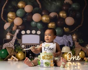 Safari themed first birthday setup with balloons and baby next to cake.