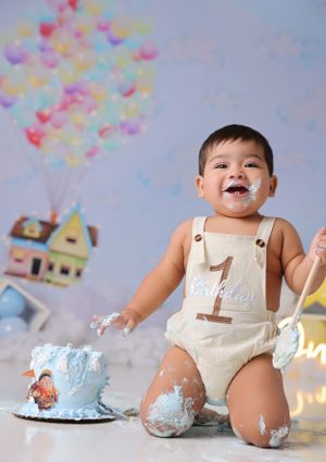 Whimsical UP movie inspired cake smash with colorful balloons and a messy blue birthday cake.