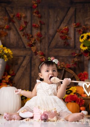 Fall-themed cake smash with rustic barn door, autumn leaves, and white pumpkin decorations.