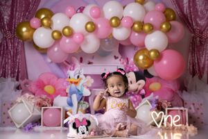 Pink and gold balloon arch backdrop with Disney-themed first birthday decorations.