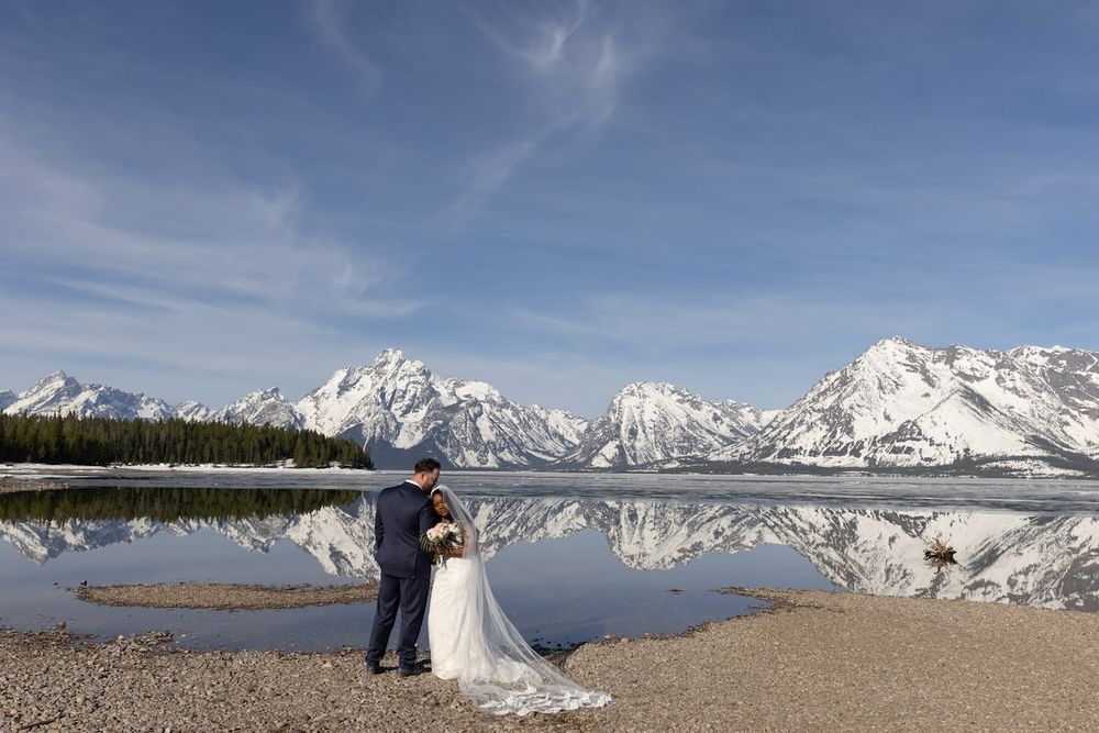 Snowy mountain peaks rise majestically behind clear blue lake waters in a stunning winter landscape.