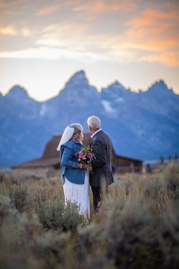 An elderly couple shares a romantic moment at sunset with the majestic Teton mountains as their backdrop.