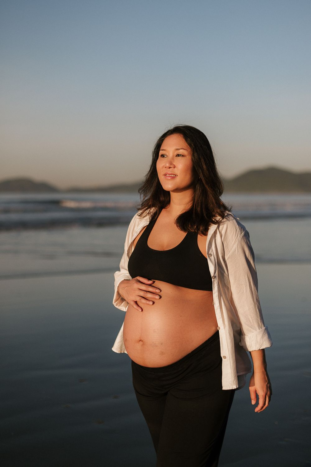 Maternity photos of woman in black outfit against serene beach backdrop.