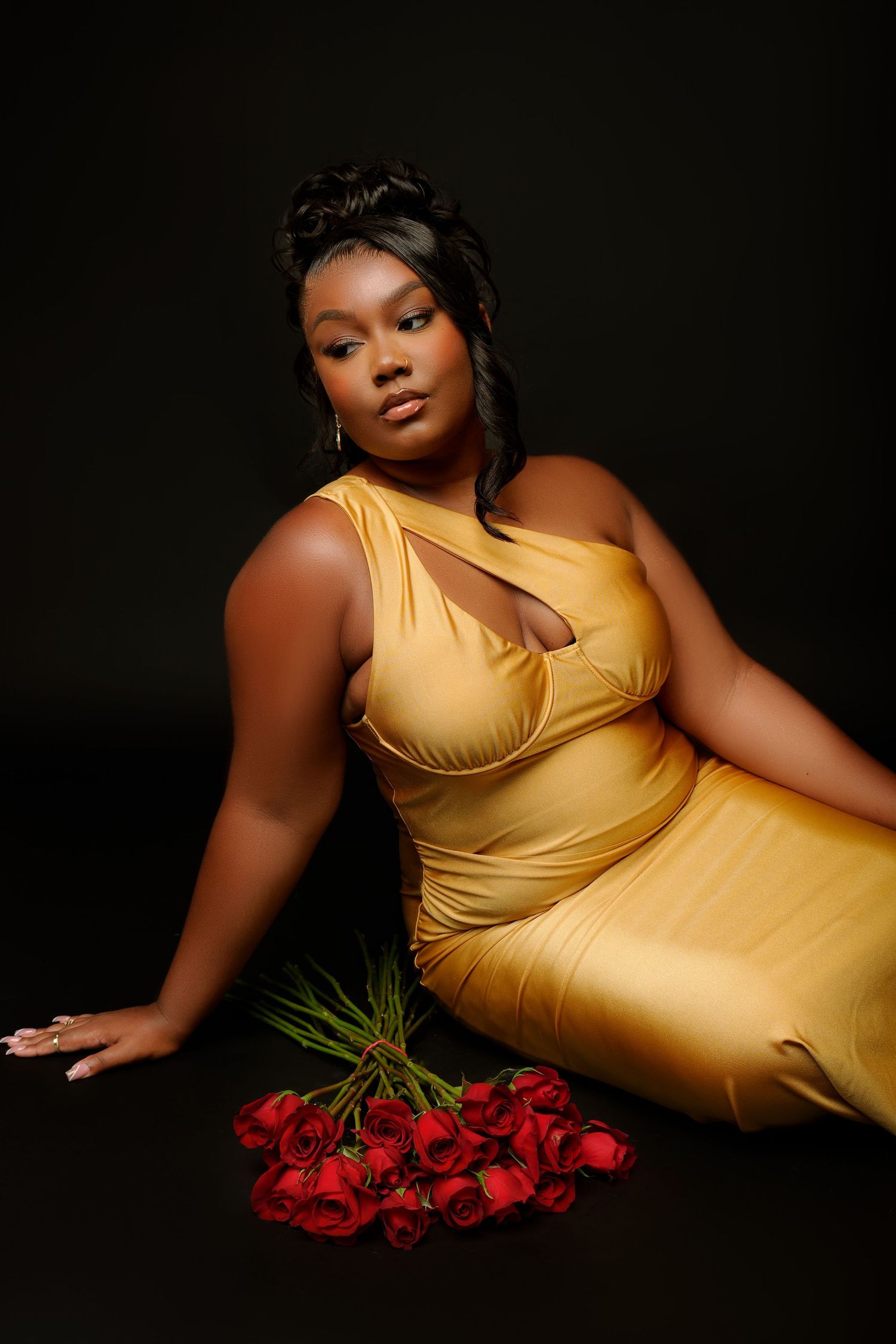 Artistic portrait with person in gold dress posing with red roses on dark background.