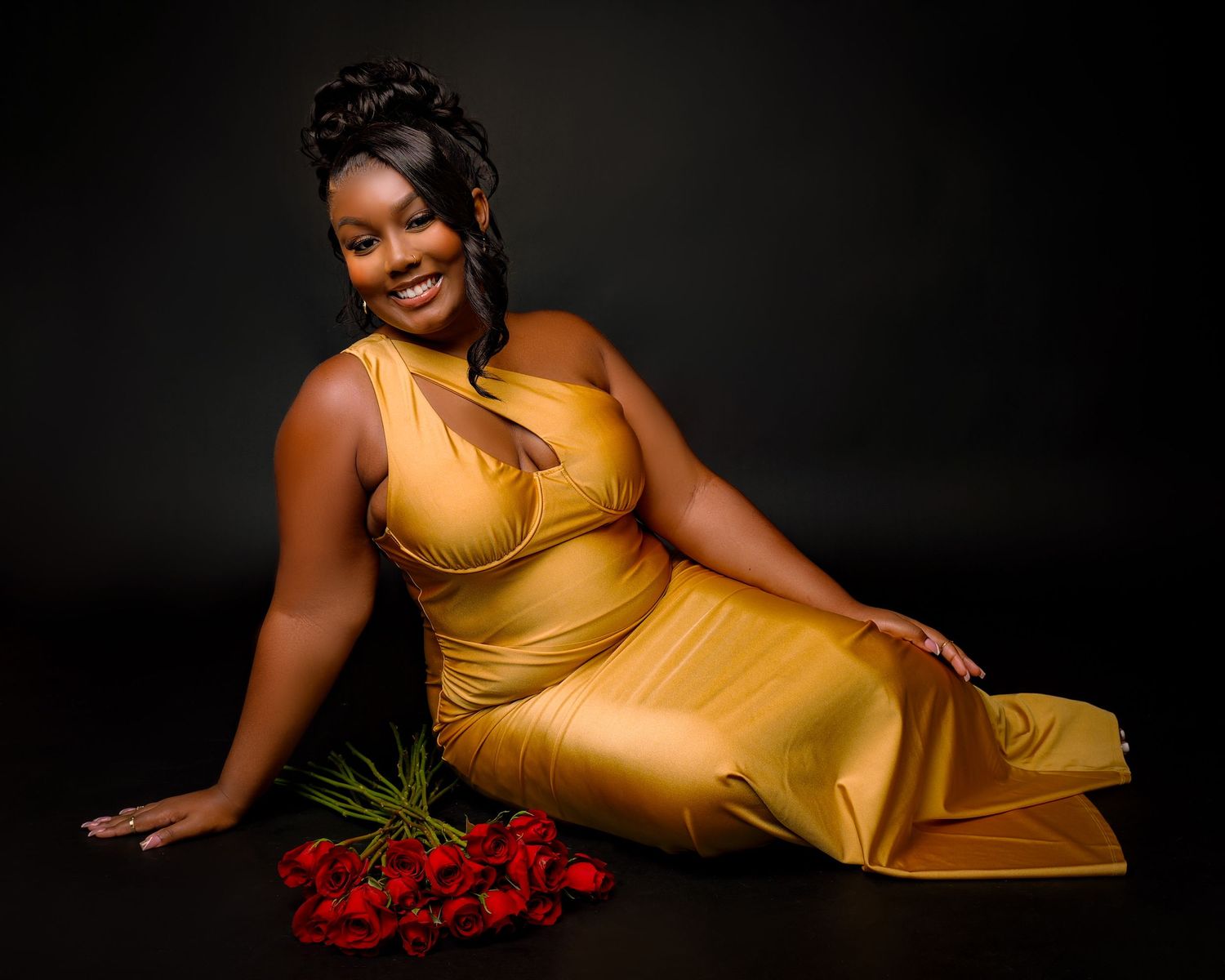 Glamorous studio portrait with person in gold dress alongside scattered red roses.