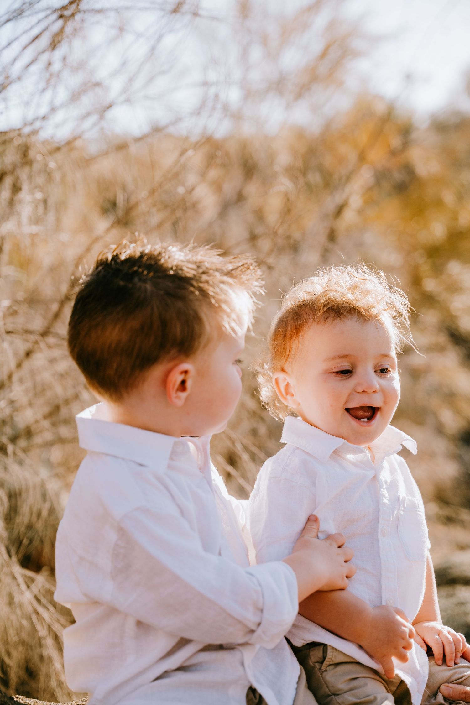 Two children in white clothing playing together in natural sunlit setting.