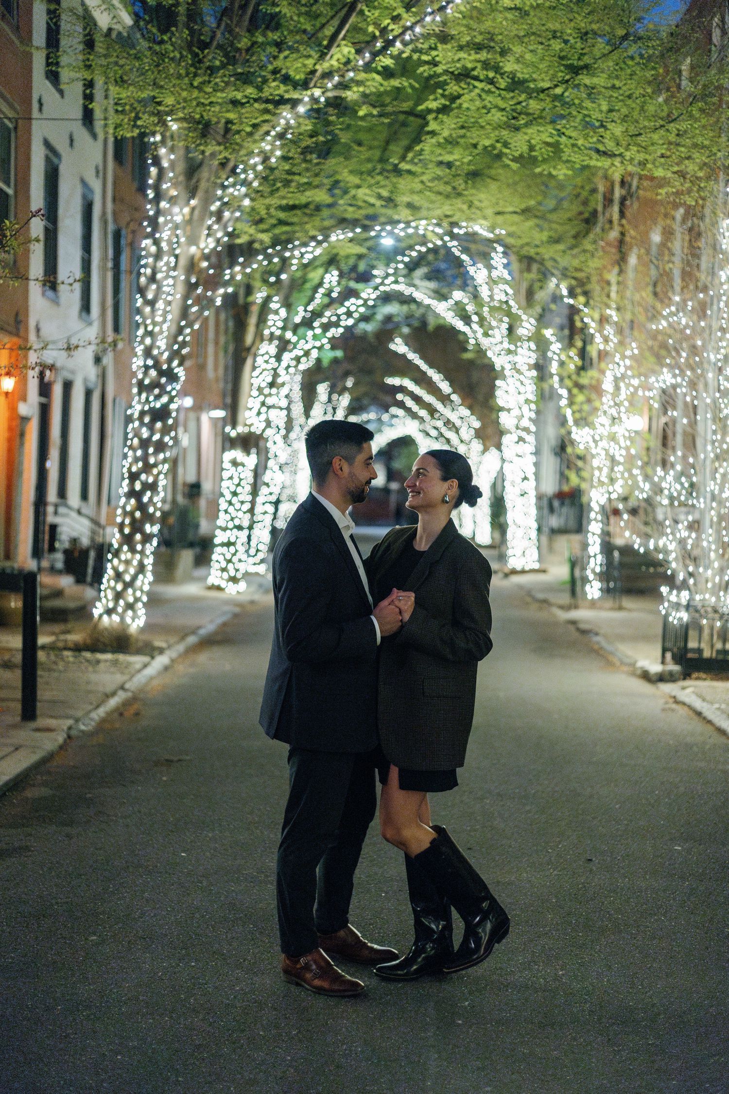 A couple shares romantic moments under illuminated trees along a park pathway at night.
