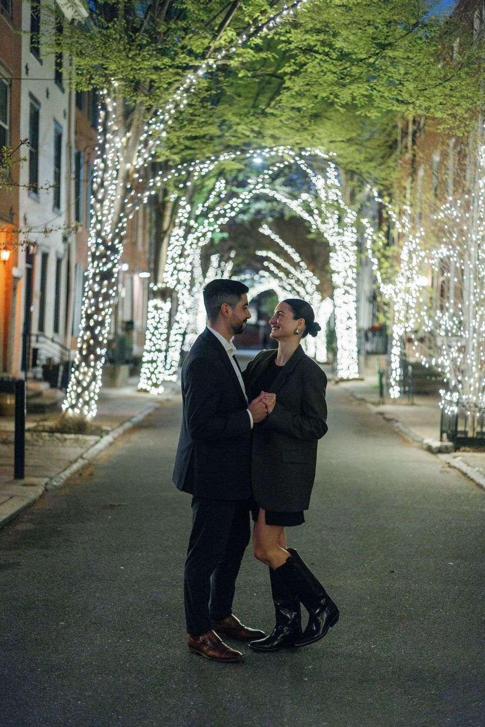 A couple shares romantic moments under illuminated trees along a park pathway at night.