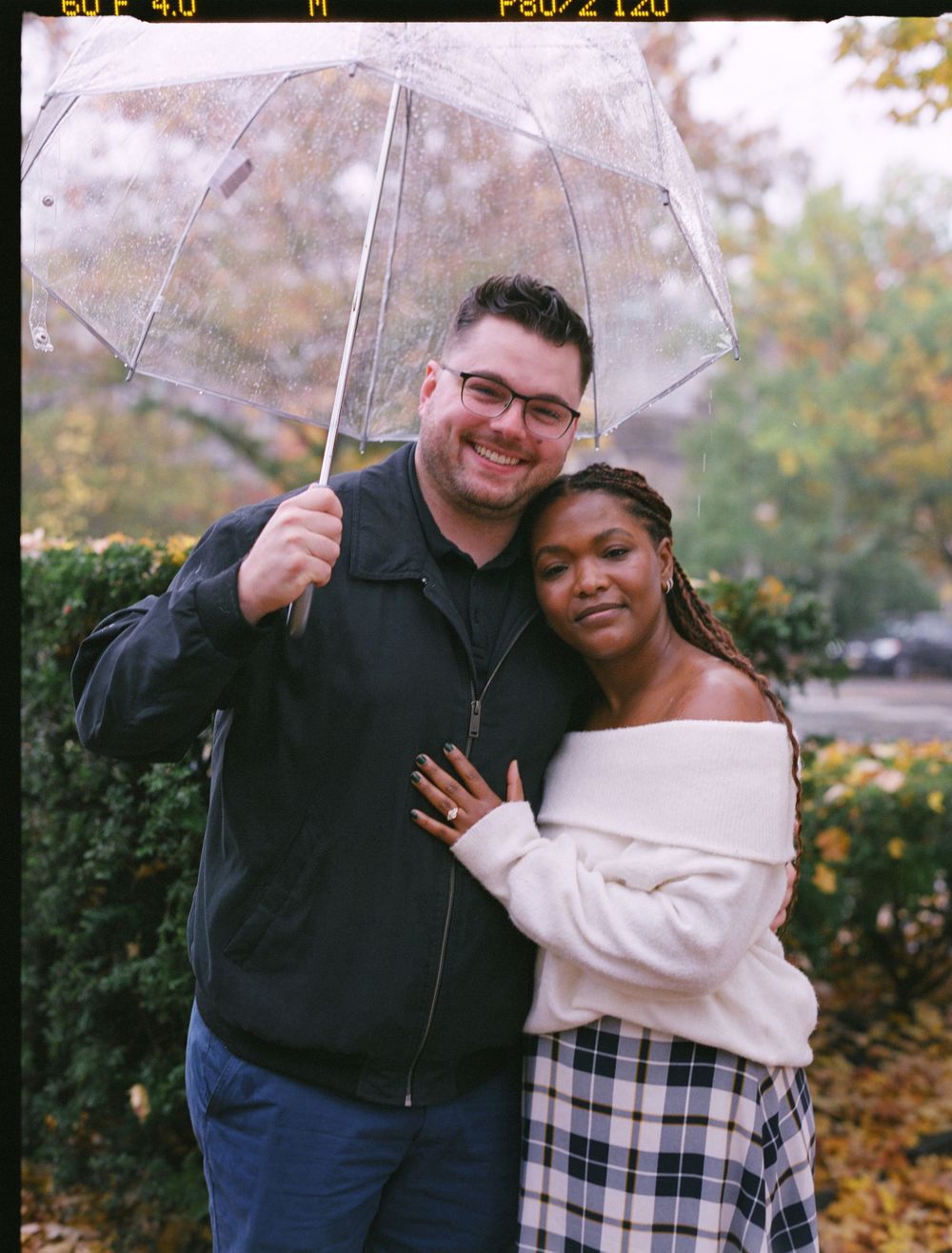 A couple shares a happy moment under a clear umbrella on an autumn day.