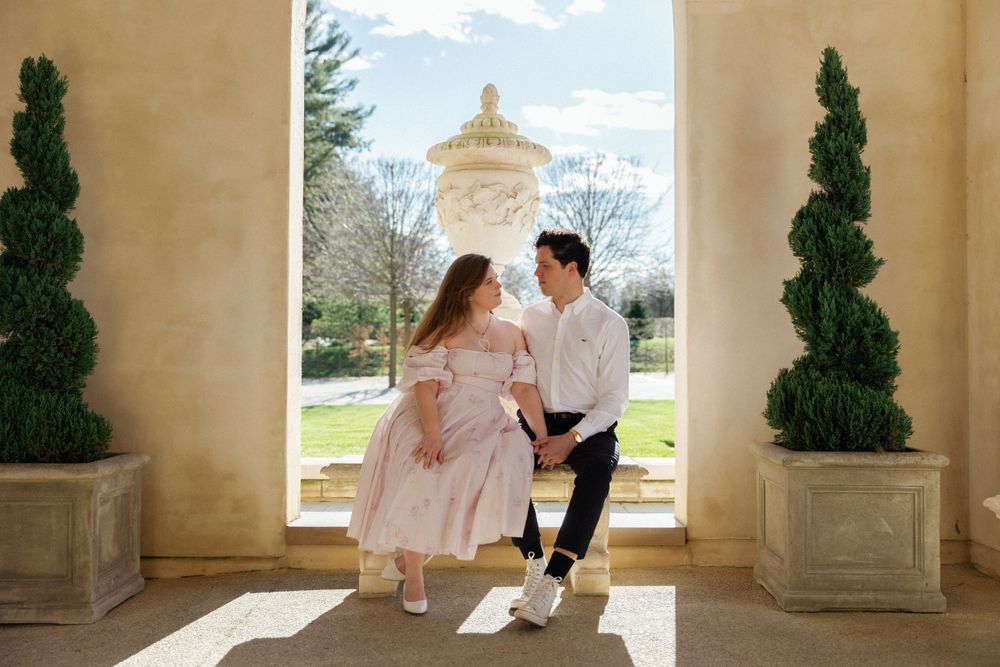 A couple dances in an elegant archway with classical architecture and cypress trees.