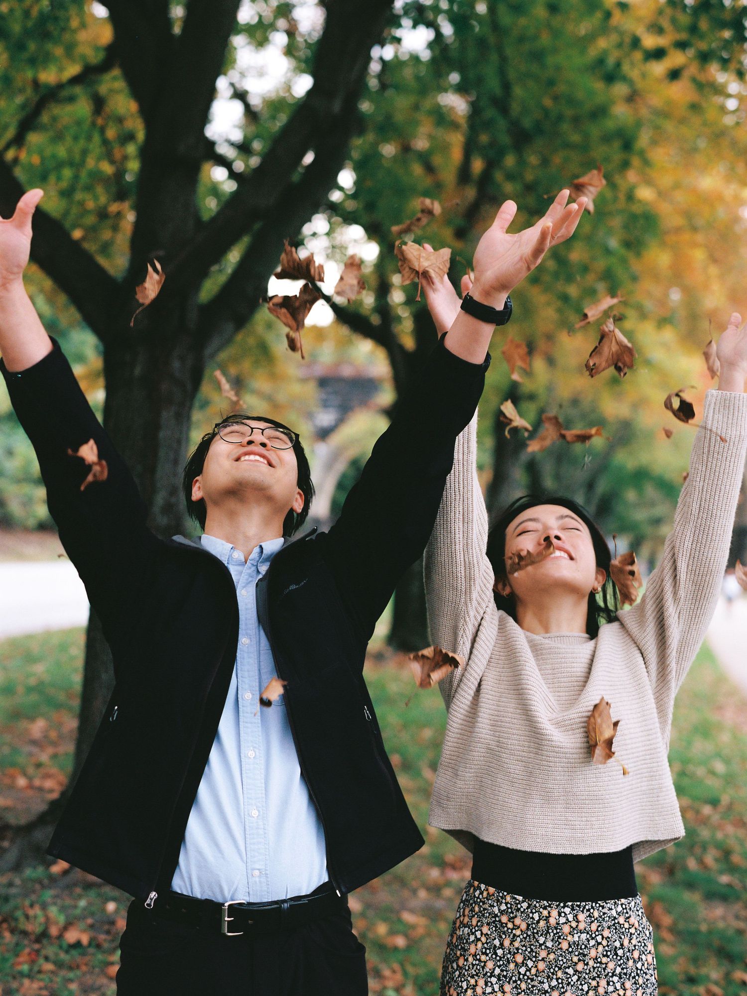 Joyful couple throwing autumn leaves in the air under fall trees.