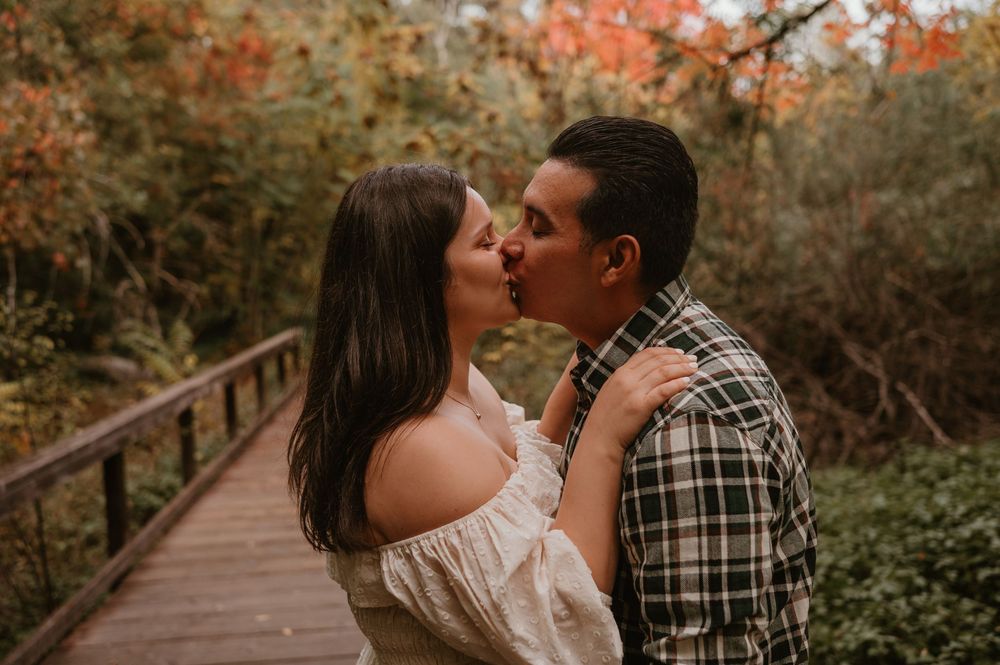 A romantic moment captured on a wooden boardwalk surrounded by autumn foliage.