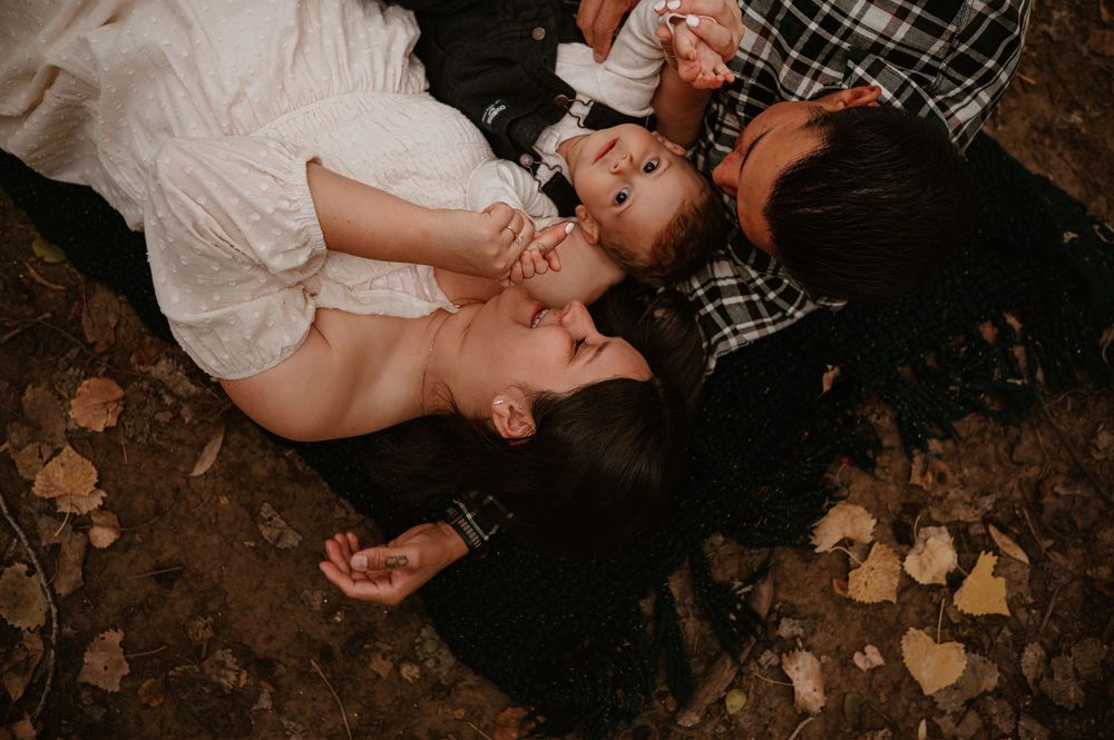 A couple shares an intimate moment while laying on autumn leaves in a romantic outdoor setting.