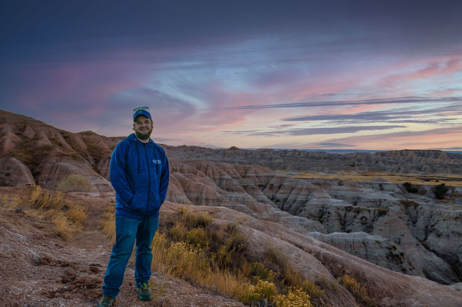 Scenic sunset view of rugged badlands formations with colorful sky and desert vegetation.