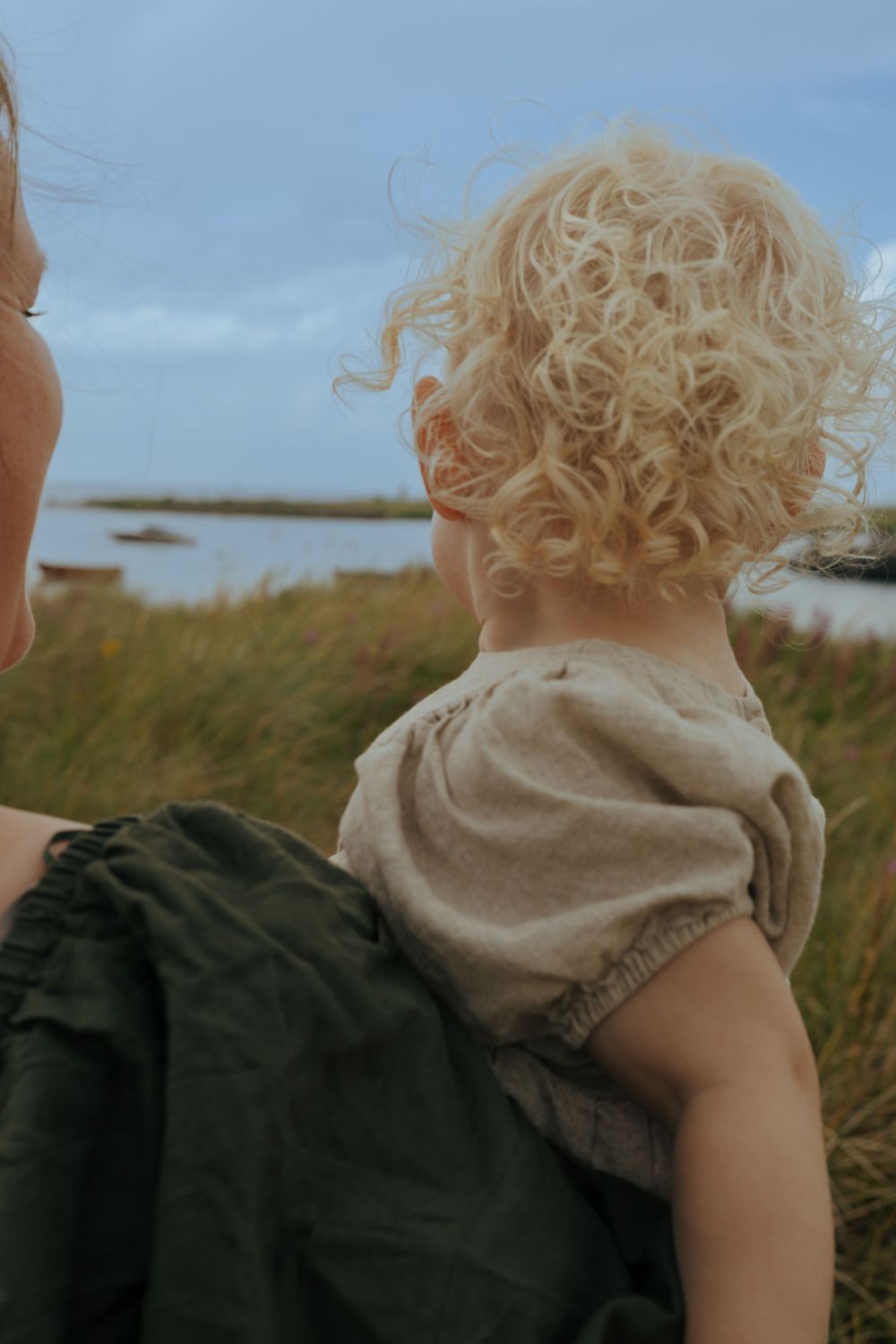 Close-up view of curly blonde hair against coastal landscape background.