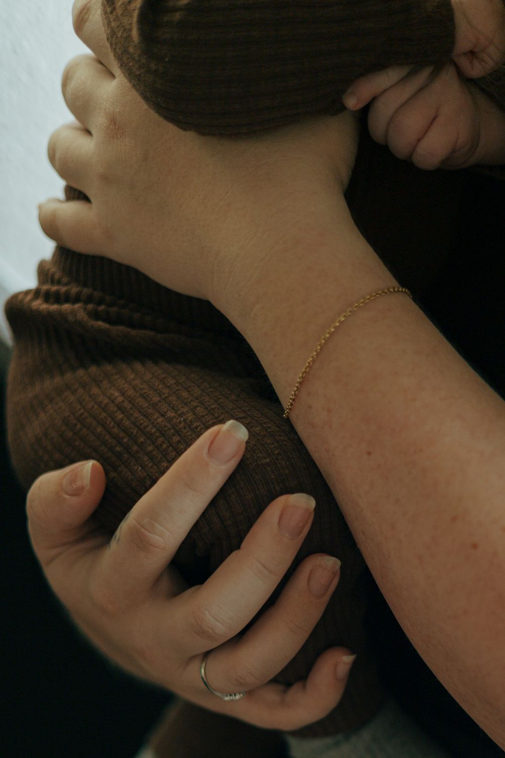 Close-up detail of hands holding baby wearing brown knit sweater.