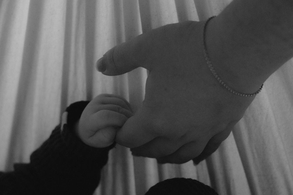 Black and white artistic photo of hands reaching in soft window light.