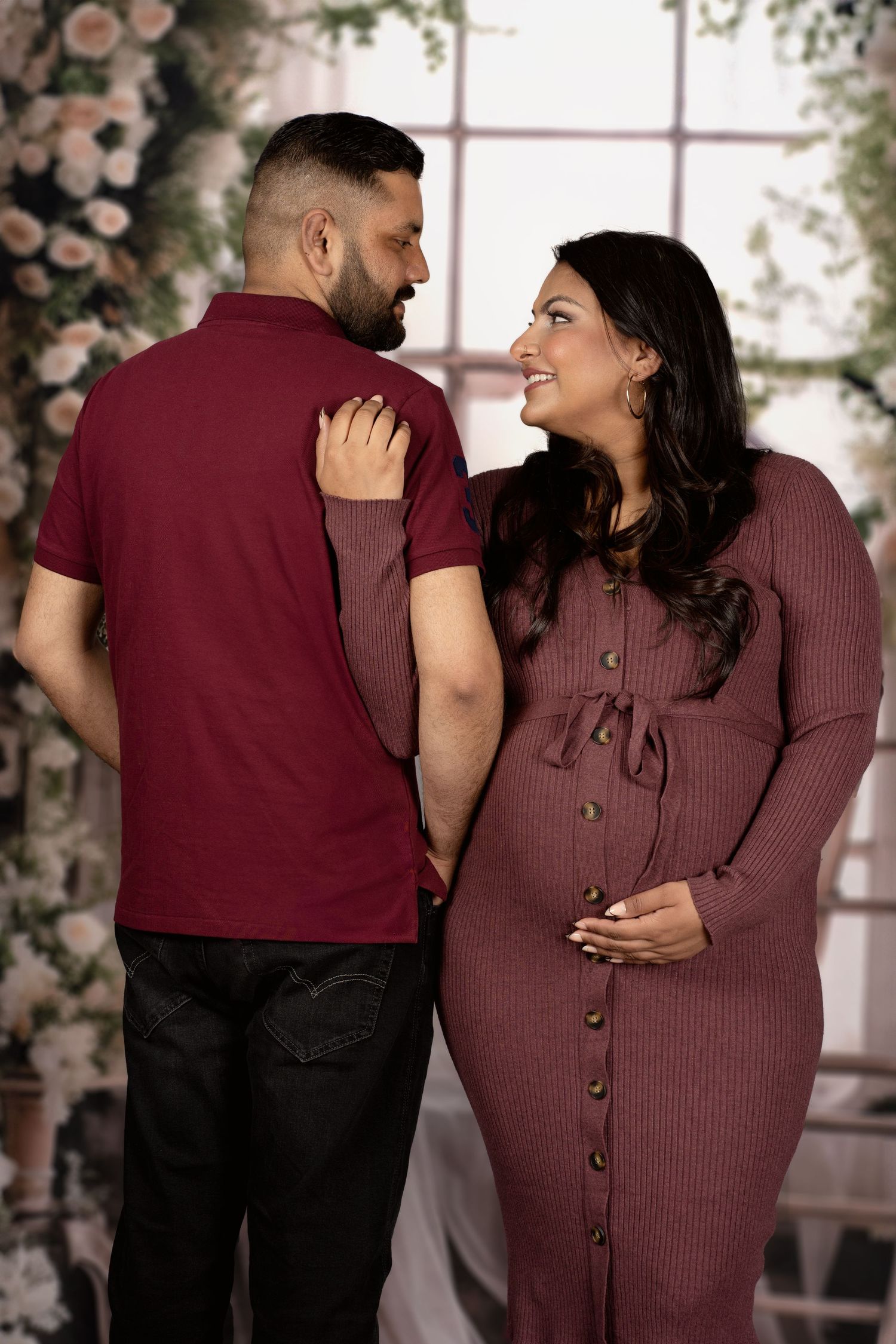 Romantic maternity portrait with couple in coordinating burgundy outfits by floral arch.
