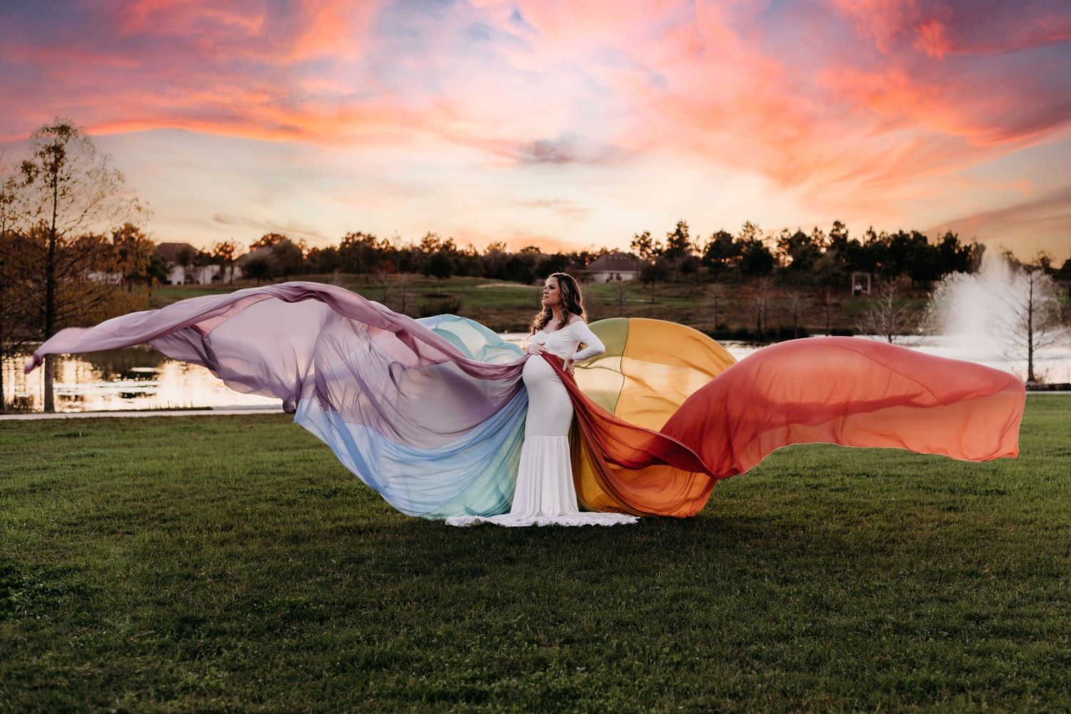 A pregnant woman in a white dress wearing a flowing rainbow overskirt