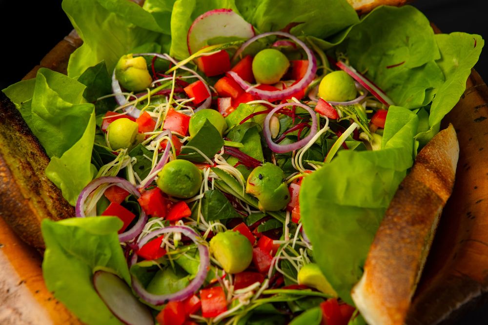Fresh green salad with microgreens, cherry tomatoes, and onion rings served on lettuce leaves with baguette slices.