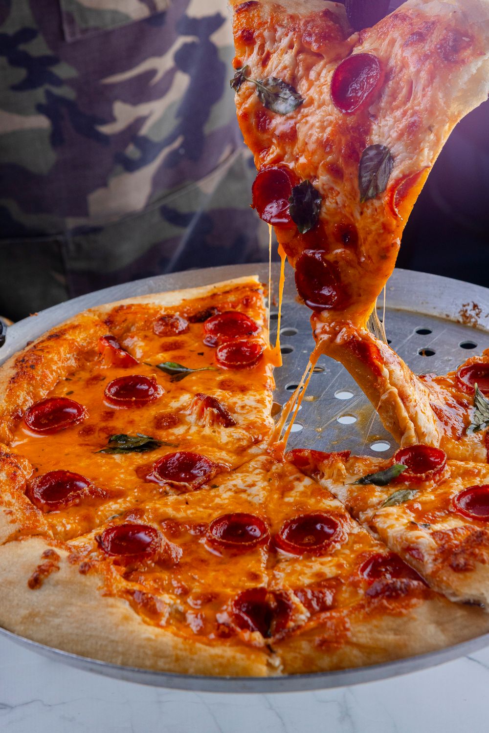 Hot pepperoni pizza with melted cheese stretching as a slice is pulled up against an American flag background.