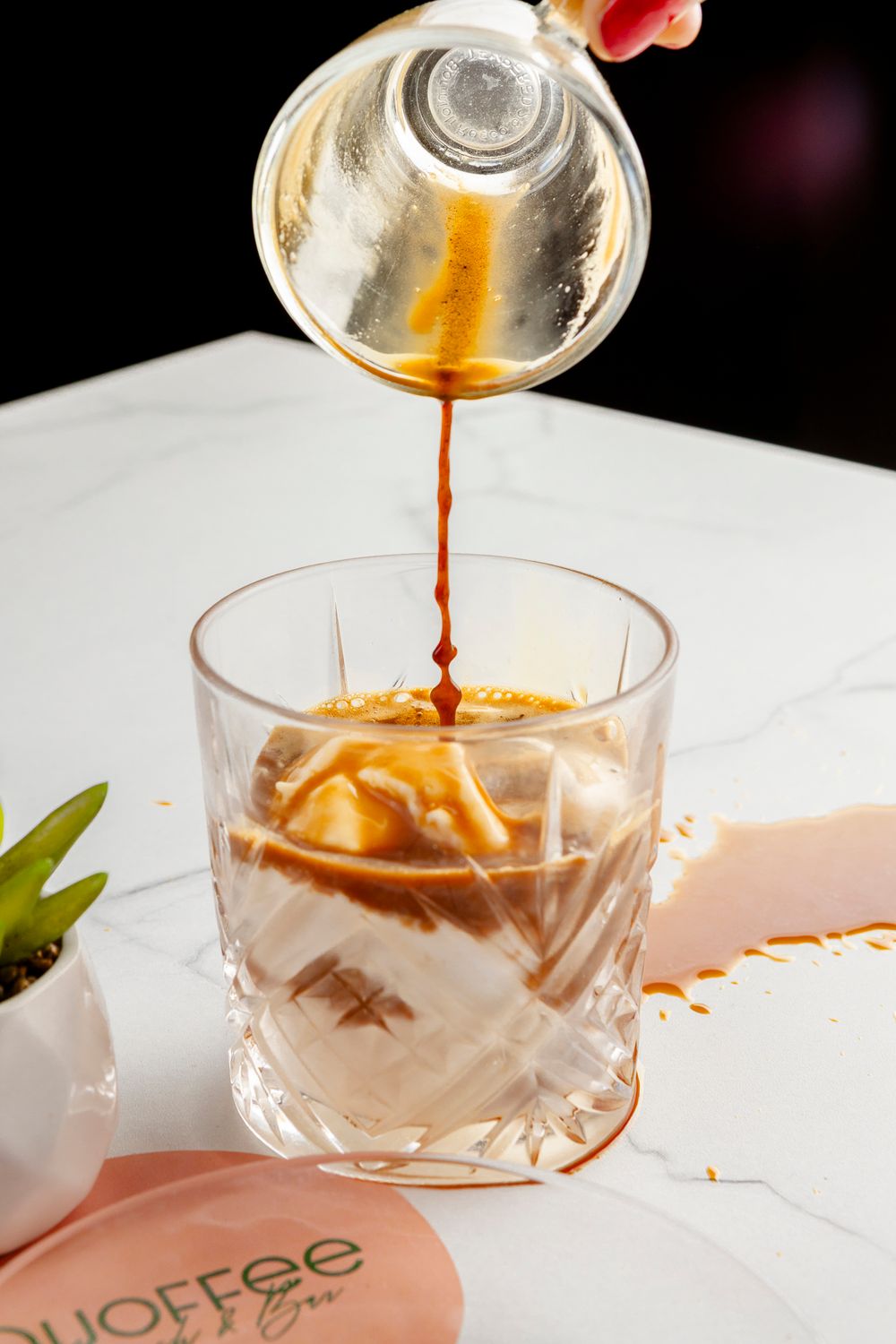 Hot espresso shot being poured over ice cream in a crystal glass creating an affogato dessert drink.
