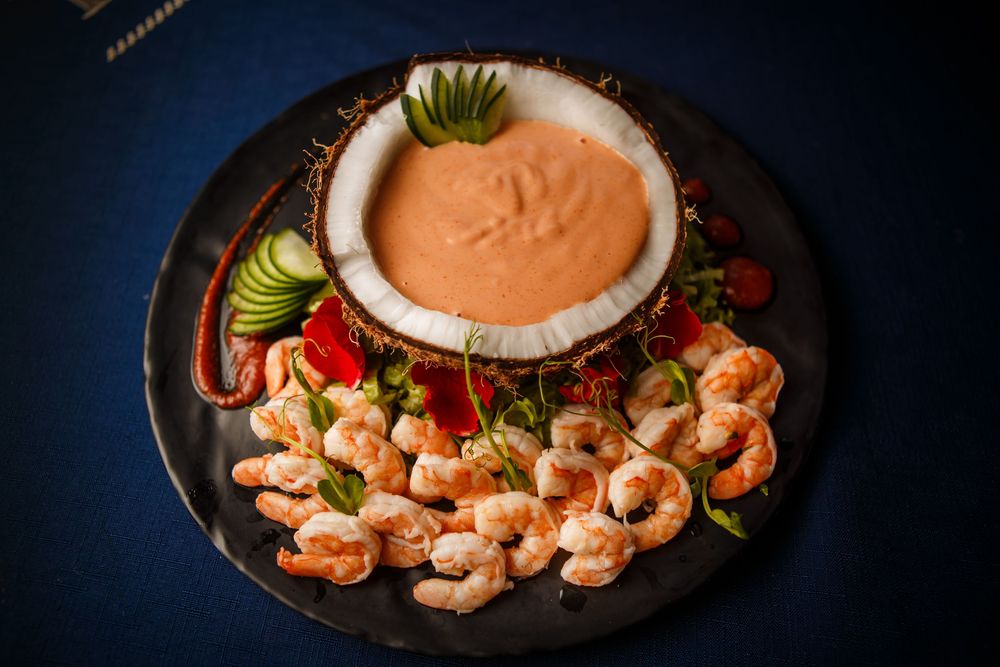 Platter of grilled shrimp arranged around a creamy pink cocktail sauce with fresh lime garnish on dark background.