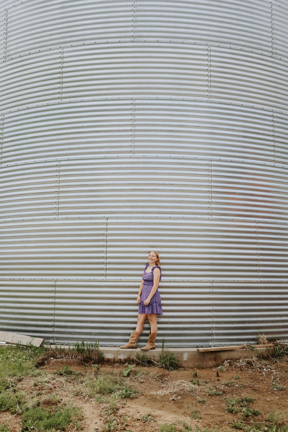 Purple dress contrasts against large metallic grain silo on a rural property.