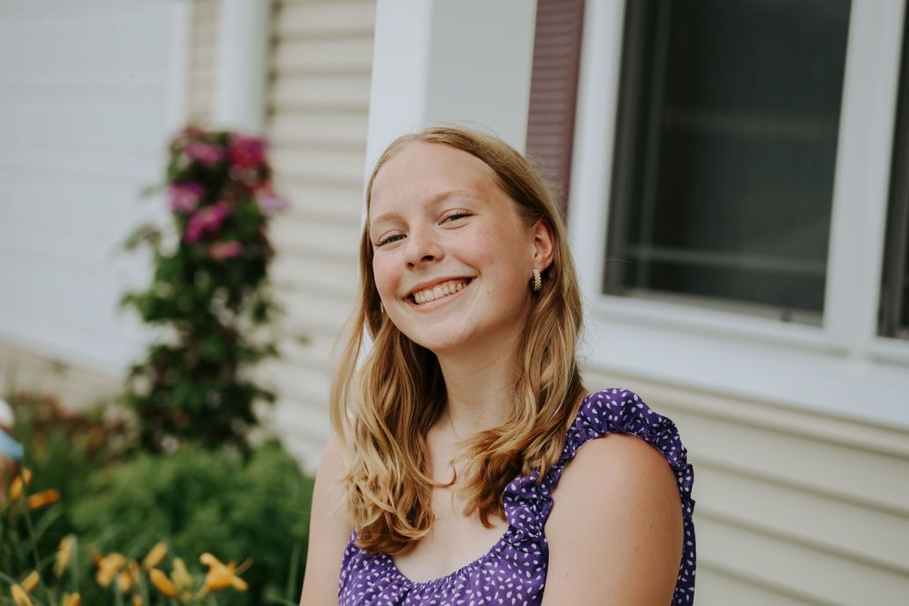 Summer portrait in a purple floral dress beside blooming garden flowers.