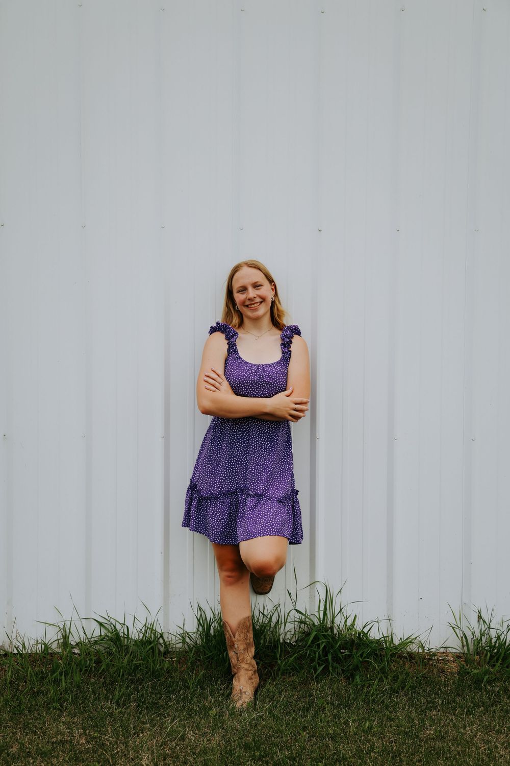 Casual portrait against white wall wearing purple floral dress and brown boots.