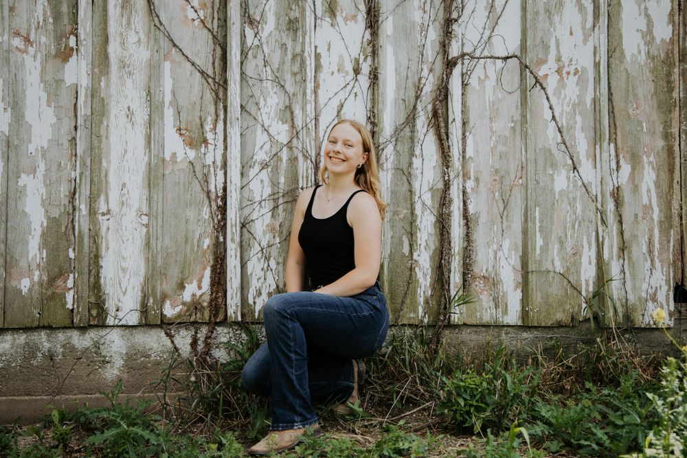 Casual portrait sitting by weathered white barn wall in black tank top.