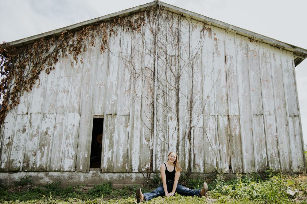Wide shot of person sitting in front of weathered white barn exterior.