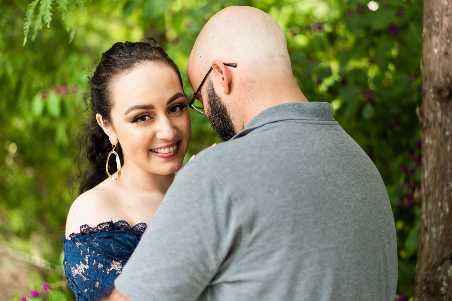 A couple shares a tender moment outdoors in a natural setting with green foliage in the background.