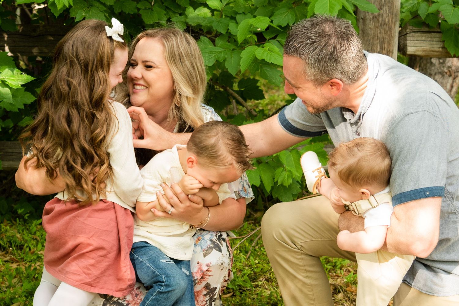 A loving family shares joyful laughter and embraces while sitting together in a lush garden setting.