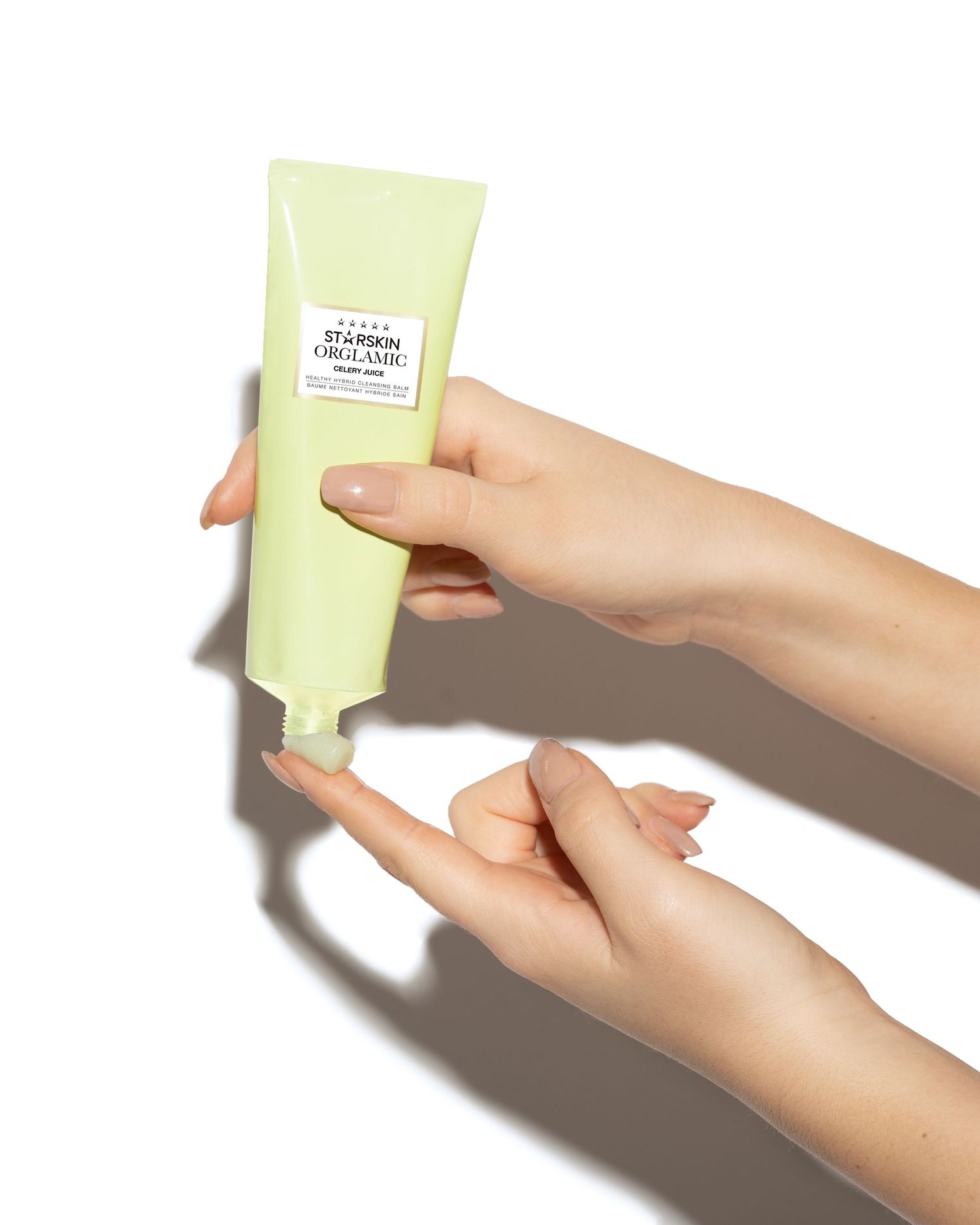 Een lichte productfoto van een beautyproduct, vrouw houdt verpakking vast tegen een witte achtergrond en smeert wat van het product op hand