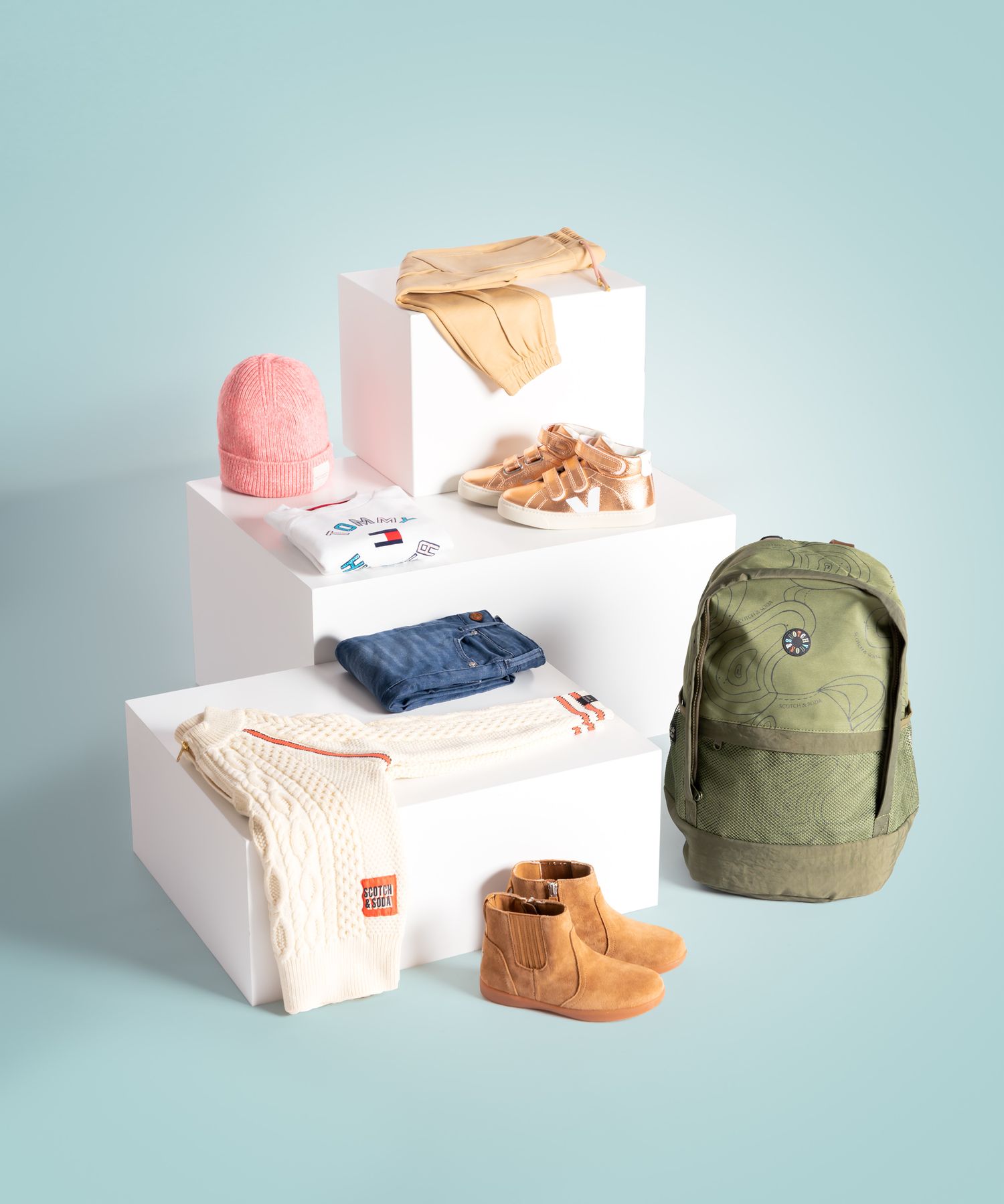 Een display met stijlvolle kinderitems, gepresenteerd op witte blokken tegen een lichtblauwe achtergrond.