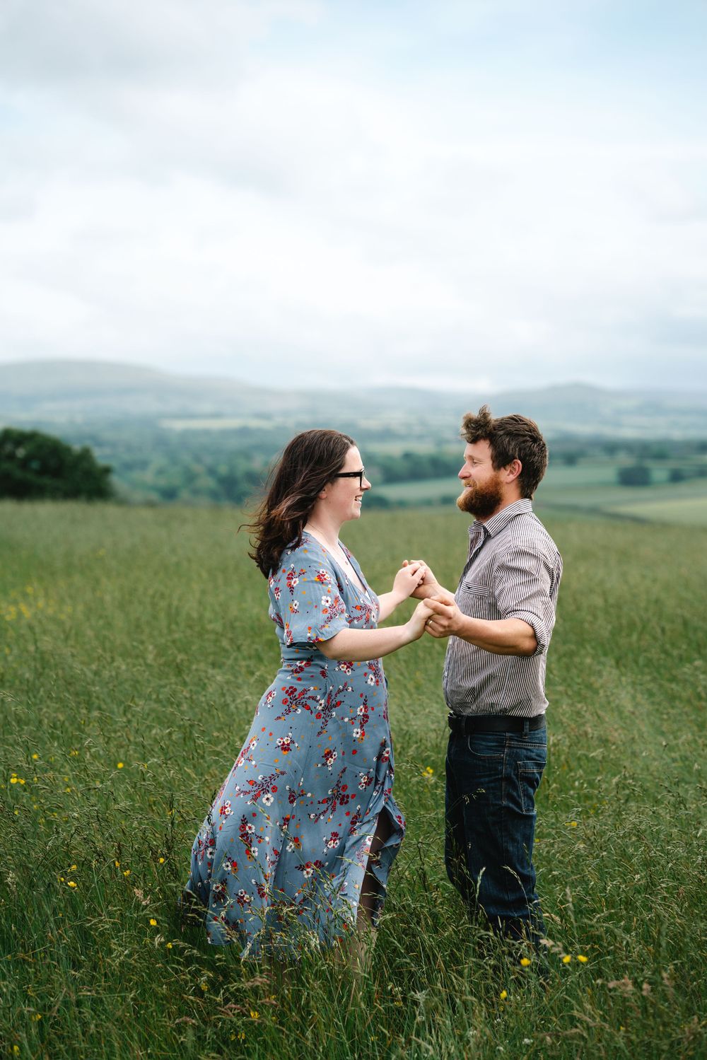 A couple dances together in a scenic meadow with rolling hills in the background.