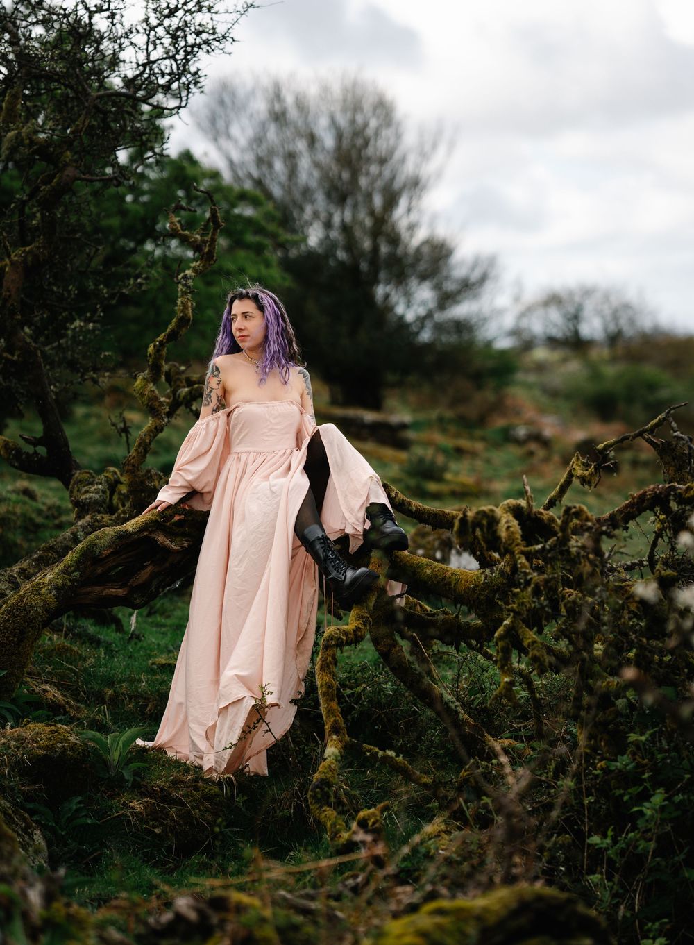 A woman in a flowing peach dress poses dramatically among mossy fallen trees.