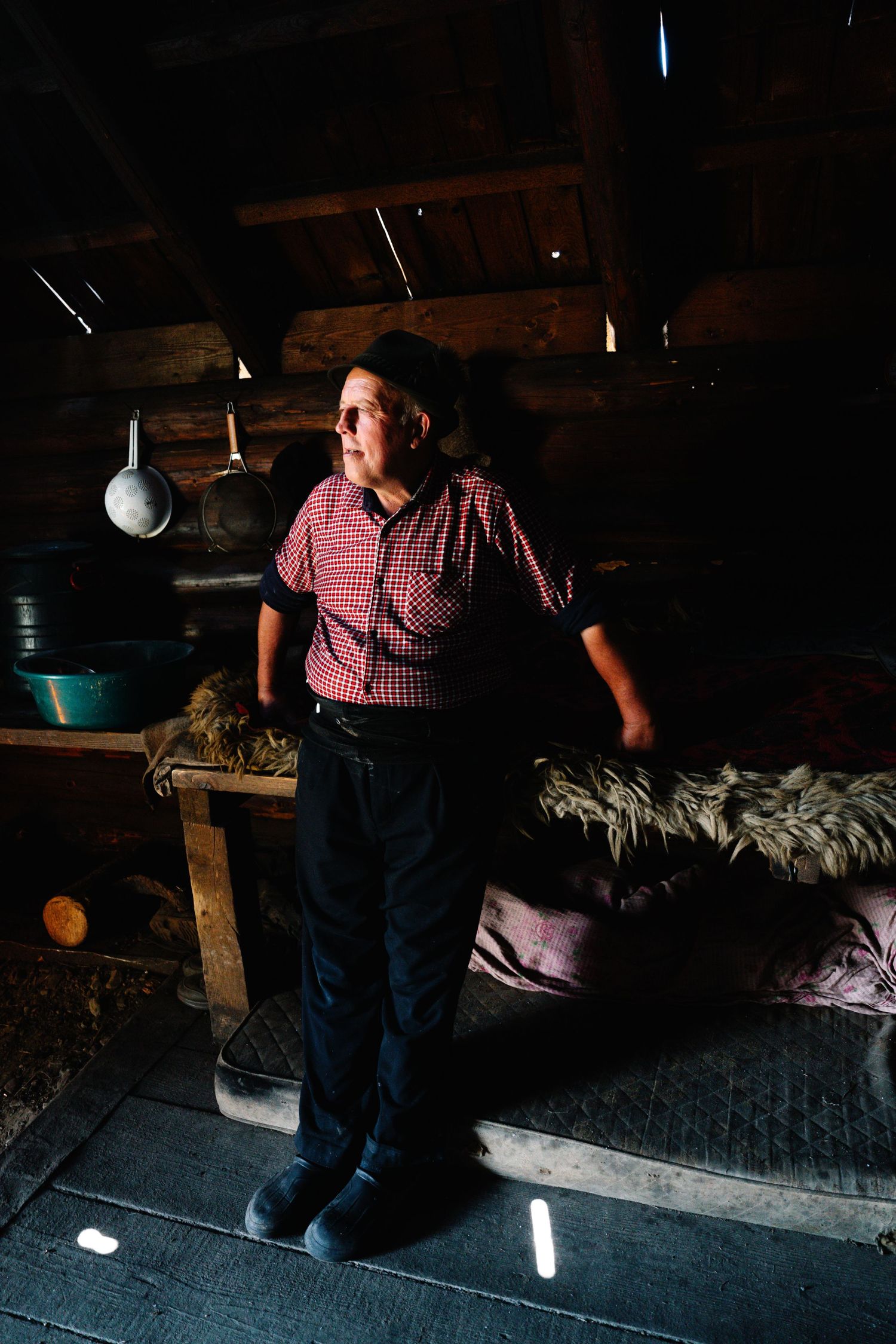 Person in plaid shirt standing in rustic cabin interior with dramatic lighting.