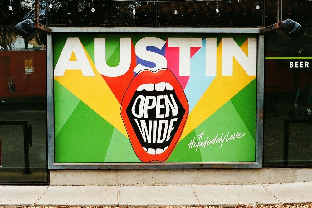 Colorful Austin Open Wide billboard sign with bold typography and graphic mouth design on a city street.