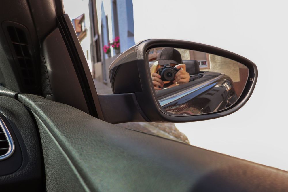 Car side mirror reflection showing interior dashboard view.