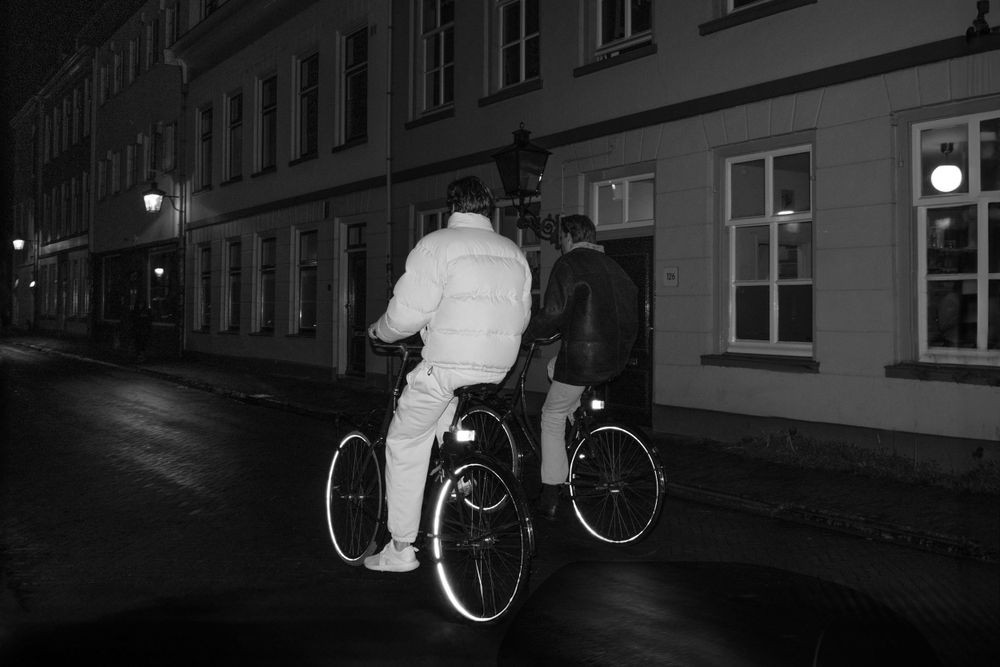 Black and white photo of cyclists riding at night on urban street.
