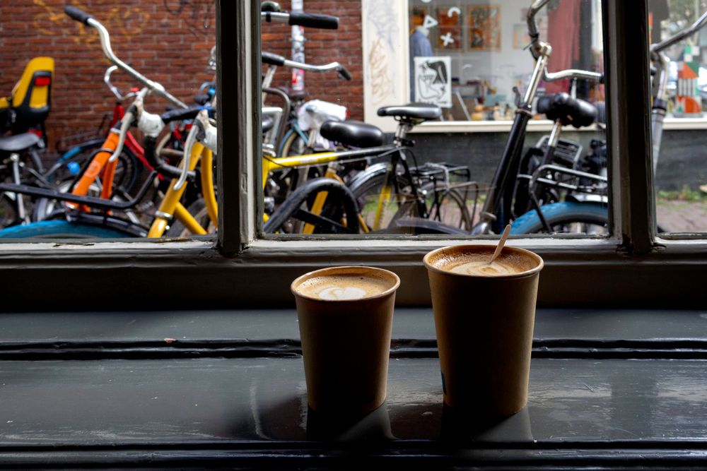 Two dark coffee drinks on windowsill with bicycles visible through glass.