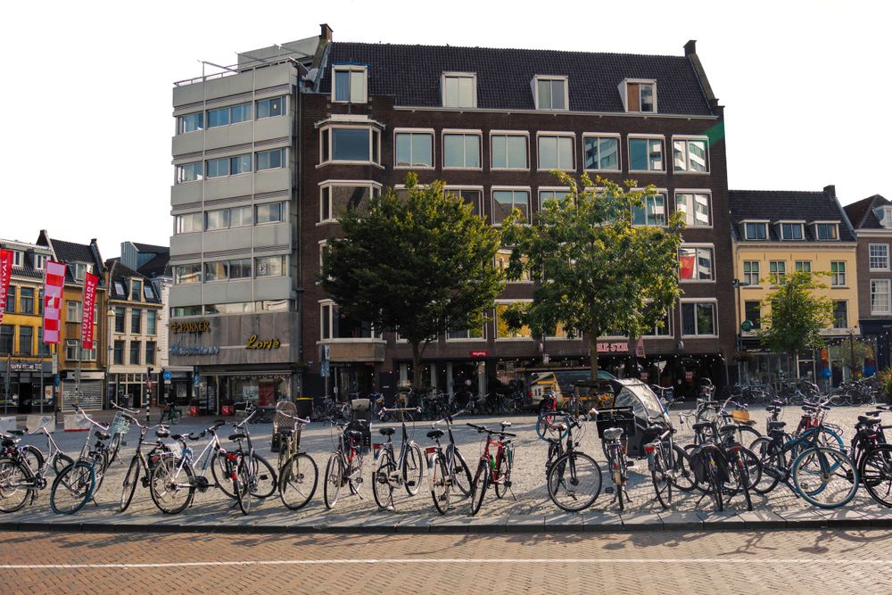 Row of parked bicycles along street with colorful European buildings in background.